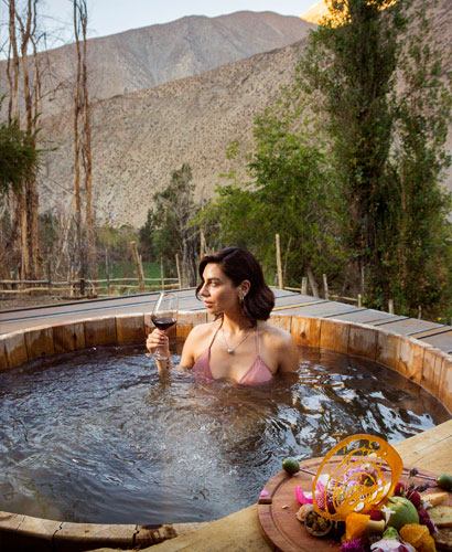 Mujer relajÃ¡ndose en una tinaja caliente en el Valle del Elqui, Chile, disfrutando de una copa de vino y una tabla de quesos.