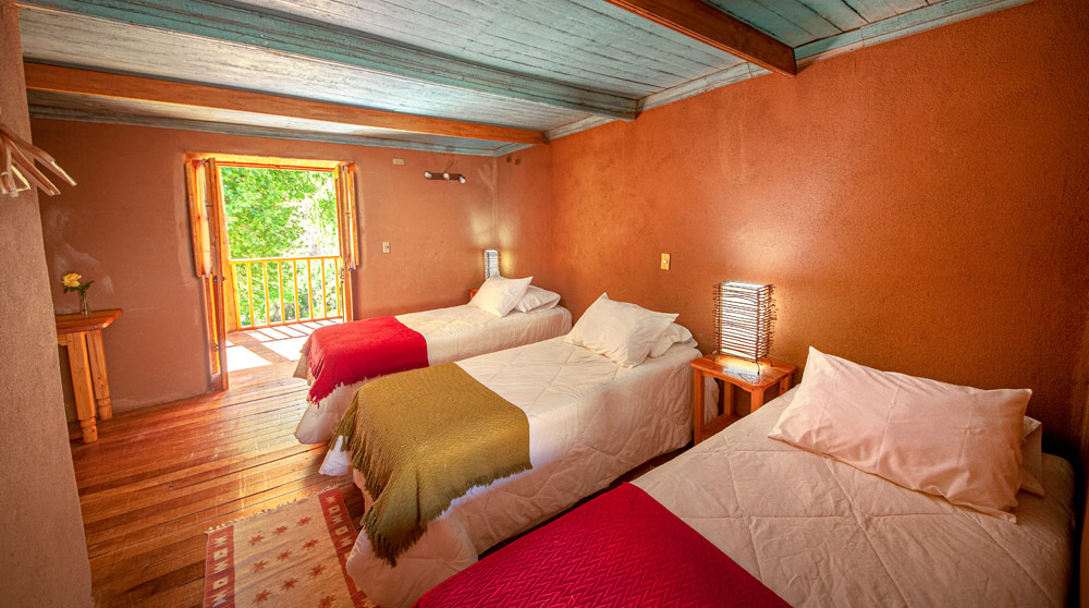 habitacion rustica con tres camas con ventanal al fondo